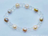 Full view of the bracelet stretches showing round translucent crystal quartz beads alternating with pink, cream, and peach freshwater pearls.