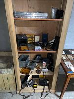 Shelf with various antique and vintage cameras, some camera cases, accessories, and photographic equipment arranged on three shelves.