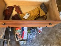 Drawer with three brown leather handgun holsters, one yellow cloth rifle sock, and various booklets and items laid in front arranged inside drawer.