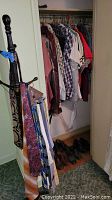 Photo showing a closet with assorted vintage clothing on hangers, shoes on floor, and multiple ties hanging on a wooden clothes tree.