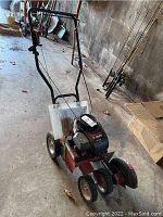 Full front view of the Troy Bilt edger showing the handle, wheels, and engine assembly with manual attached.
