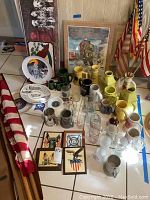 Overview of collection including multiple fire company mugs in ceramic and glass along with decorative plates and plaques and flags in background