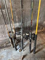 Six fishing rods standing upright, five with reels, one without. Rods show signs of use and need cleaning.