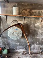 Photo showing galvanized watering can on shelf, vintage scythe hanging with long wooden handle and two grips, and galvanized tub mounted on wall hooks with concentric circles visible.