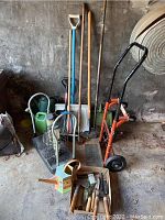 Wide view of the lot showing the hand truck, garden tools, watering cans, bird feeders, and box of hand tools in garage against concrete wall.