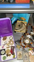 Overview of assorted watches, jewelry, awards and necklace in a collection spread on a surface.