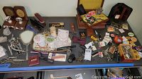 Photo showing assorted keys, pins, vanity items including hand mirror with floral design, metal scissors, wooden boxes, and small trays.