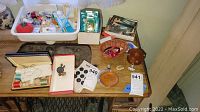 Displays the various sewing notions on a wooden table including trays with threads, buttons, and sewing accessories