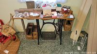 Front view of antique Singer sewing machine base with wooden tabletop, wood drawers underneath, and black cast metal treadle base with pedal.