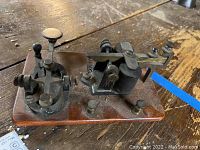 Photo showing metal telegraph key mechanism mounted on wooden base from an angled top view.