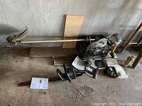Photo showing Echo gas grass trimmer with long metal shaft and cutting head, and Craftsman hedge trimmer with 20-inch red blade and black handle, along with manuals and tools on the floor.