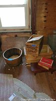Remington wooden box with lid, vintage wooden crate, cigar boxes, partial view of small wooden stool and barrel table top inside cabin or wooden room with natural light.