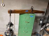 Wood yoke with two vintage Dietz lanterns attached hanging on a green filing cabinet. Shows the yoke length, and lantern details.