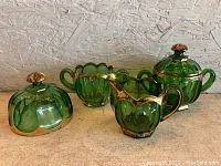 Green antique Victorian glass dishes including covered sugar bowl, creamer, and two-handled bowl with gold trim