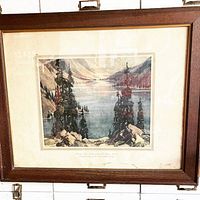 Full view of framed antique print showing landscape of Moraine Lake with surrounding mountains and trees.