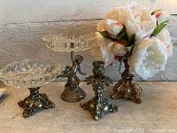 Four Hollywood Regency style pieces including two tiered glass dishes on metal bases, one held by a mermaid figure, and a pair of metal candle holders/flower holders.
