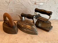 Photo of three vintage flat irons with wooden handles arranged side by side on table.