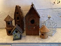 Image showing six birdhouses arranged on a surface including wooden and wire designs with different roof shapes and colors.