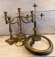Group photo showing all four brass candle holders and the brass horn together on a light-colored surface against a textured wall.