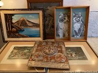 Shows overall arrangement of art pieces including framed paintings of mountain landscape and kittens, metal relief plaque, and two prints