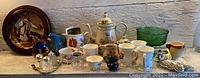 Overview of various vintage ceramic dishes and cups, green glass bowl, decorative plate, and teapot.