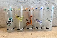 Photo showing the full set of five frosted glasses with circus animal designs lined up against a textured wall.