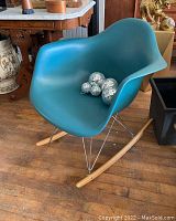 Front and side angle of turquoise plastic molded seat rocking chair with chrome wire base and wooden rockers. Mirror balls on seat not included.