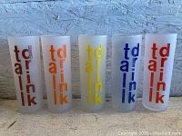 Front view of all five frosted Morgan drinking glasses in a row showing 'tall drink' text in different colors: brown, orange, yellow, blue, red