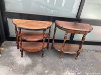Two vintage wood side tables shown together outdoors on concrete, featuring curved tops and lower shelves.