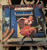 Front cover of the vinyl album with Cyndi Lauper in a red dress in front of a blue wall.