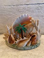 Front view showing the full seashell arrangement around the lamp base with palm tree and coral details.
