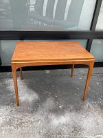 Full view of the rectangular walnut coffee table with four tapered legs outdoors against a windowed backdrop.