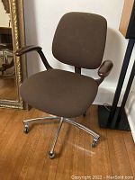Front and side view of the vintage office chair showing brown fabric upholstery, wooden armrests, and metal base with wheels.