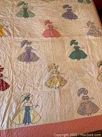 Full view of quilt with various girls in bonnets appliquéd all over front with pink border.