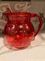 Red translucent plastic Kool-Aid pitcher with smiling face, shown alone on countertop