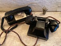 Black vintage rotary dial desk phone and black candlestick phone with braided cord on tabletop