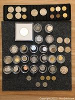 Full view of assorted coins spread on a mat, showing coins in protective holders, capsules, and loose coins including various sizes and metals.