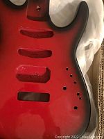 Close-up of the red sunburst Strat style guitar body showing pickup and control cavity routings, finish and contour.