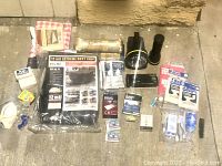 Emergency kit items arranged on ground including duct tape, masks, flashlights, water packets, tarp, rope, and assorted small supplies
