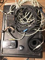 Lot includes multiple guitar cables (coiled and straight), a black Fender guitar tuner, guitar hanger, guitar picks and pick holder, all placed on a surface.