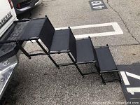 Side view of fully extended four-step retractable pet stairs showing black metal frame and fabric steps.