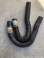 Two black flexible corrugated sewer hoses coiled forming a 'U' shape with Rhino Flex labels visible on each hose.