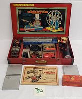 Full view of red metal case open showing included parts, lid artwork and instruction booklet.