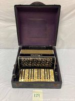 Image showing black and gold accordion inside open black hard case with purple interior lining