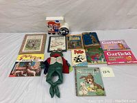 Overview photo showing 11 vintage children's books arranged on a white backdrop with Raggedy Ann and Andy doll or clock figure in front center.