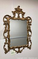 Full view of ornate gold gilt framed wall mirror hanging on white wall.