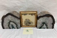 Full view of two sliced geodes flanking a framed fossil art piece on a white background with a small paper label marked '3'.