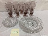 Full view of 8 amethyst goblets, 1 small amethyst glass, 1 large cut crystal plate, and 1 smaller cut crystal dish on white background.