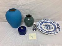 Full lot view showing all items on white cloth background including vases, wall plate, small round pottery piece, and small ceramic candle holder.