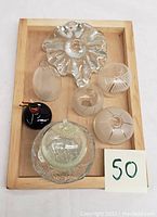 Top-down view of six glass pieces on a wooden tray: a clear scalloped candle holder, multiple textured glass balls including frosted and patterned ones, and a black glass ball with red and orange accents.